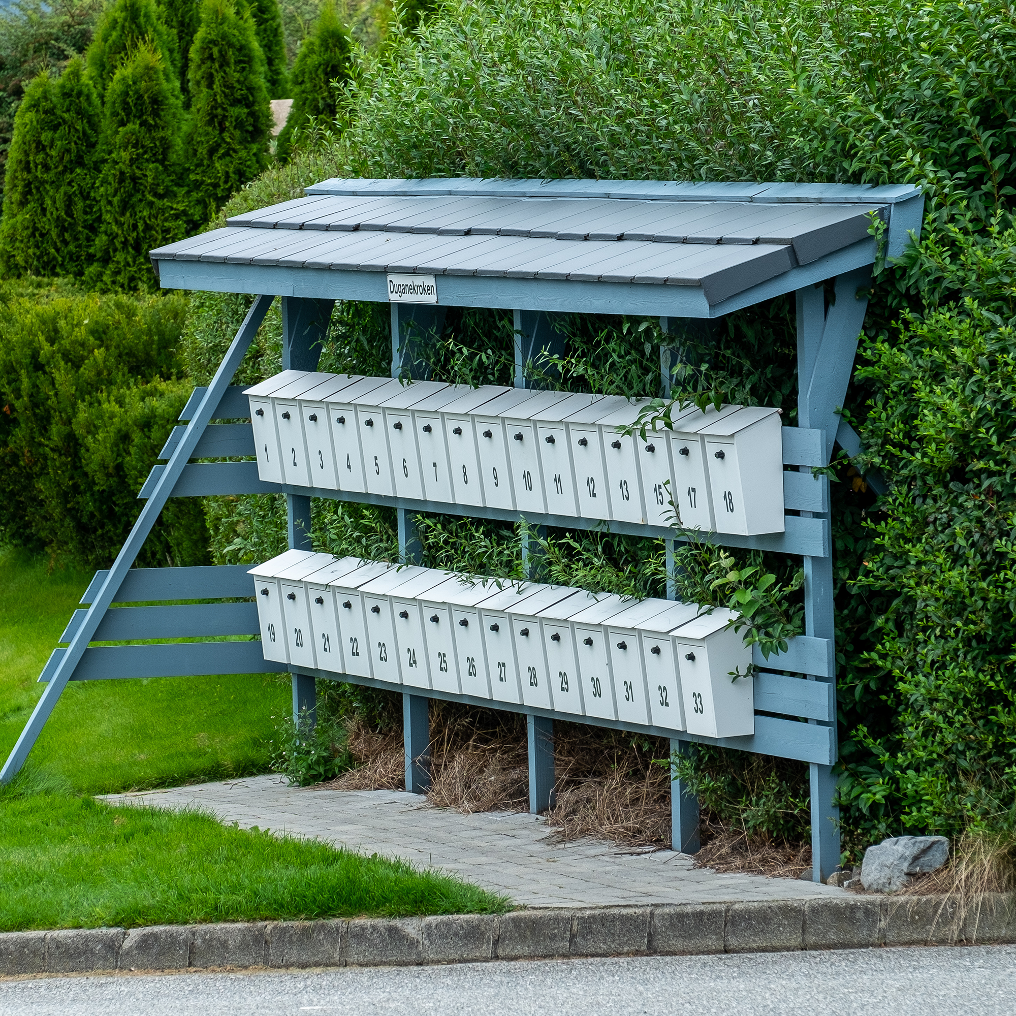 Bilde av et postkassestativ foran en grønn hekk
